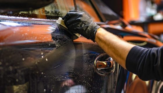 Person wearing black gloves cleaning and detailing a car body with a sponge and soapy water