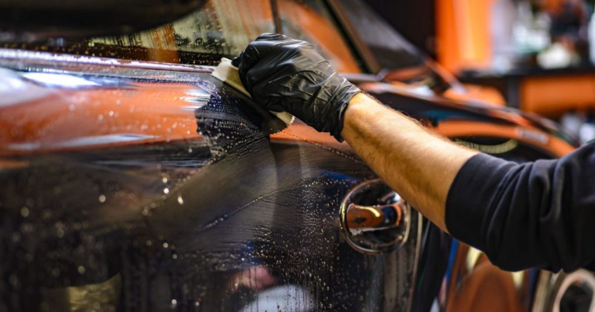 Person wearing black gloves cleaning and detailing a car body with a sponge and soapy water