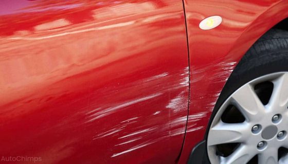 Severe scratch damage on a red car's side panel and wheel arch.