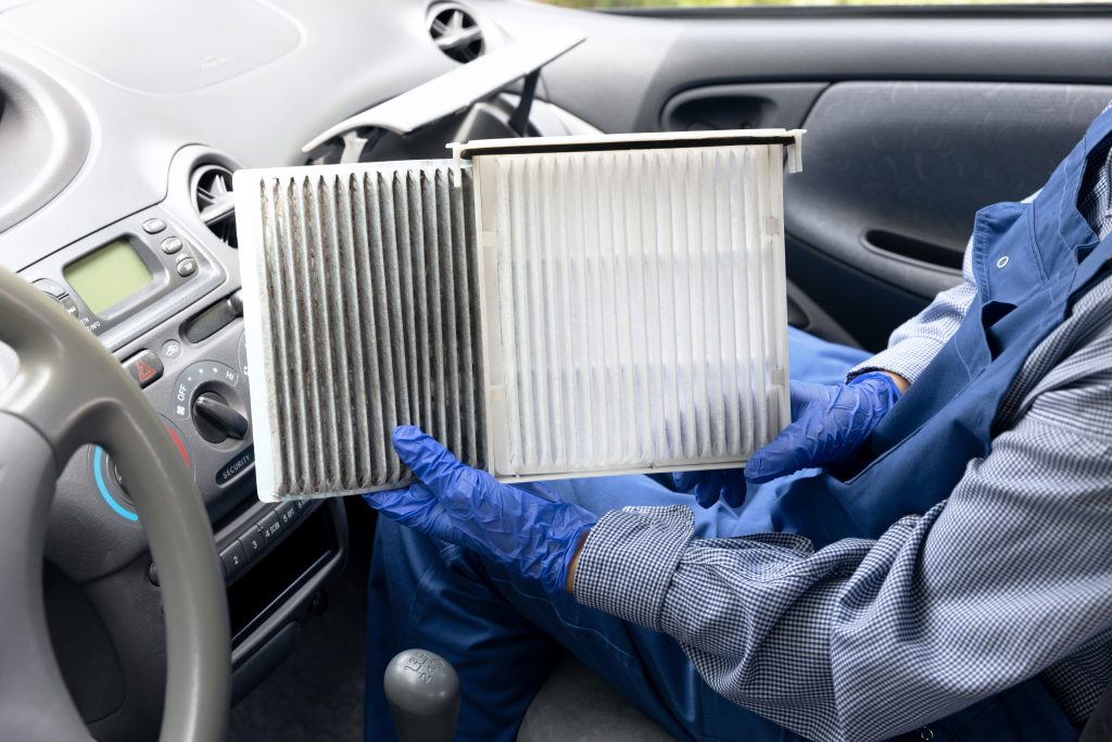 Side-by-side comparison of a dust-covered dirty cabin air filter and a clean new filter inside a car dashboard area