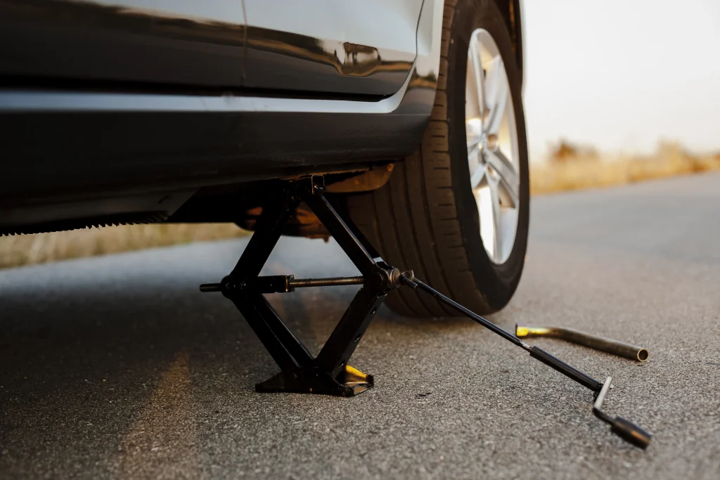 Scissor jack lifting a black car frame off the ground as part of how to change a car tire.