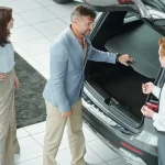 A couple in a showroom checking the open trunk space of a vehicle while learning about different car body types from a salesman.