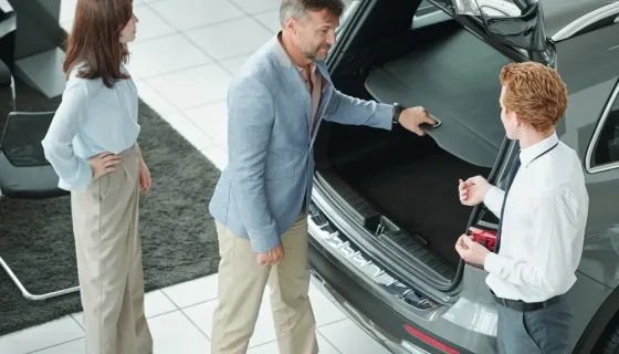 A couple in a showroom checking the open trunk space of a vehicle while learning about different car body types from a salesman.