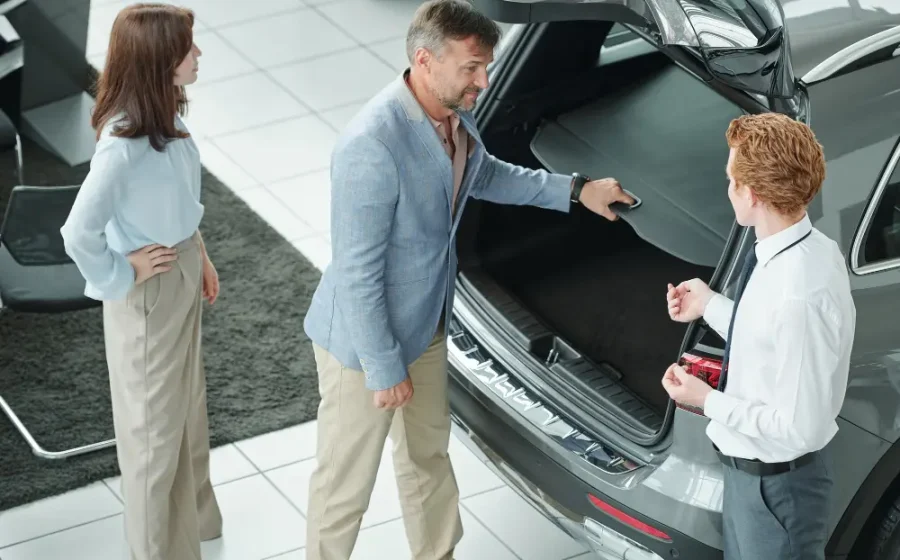 A couple in a showroom checking the open trunk space of a vehicle while learning about different car body types from a salesman.