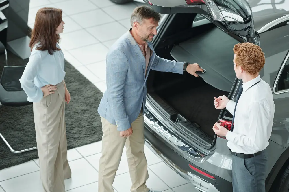 A couple in a showroom checking the open trunk space of a vehicle while learning about different car body types from a salesman.