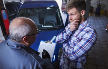 Mechanic taking notes on a clipboard while helping a customer check for a car recall.