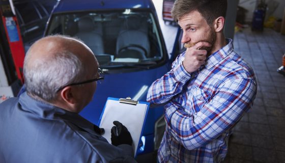Mechanic taking notes on a clipboard while helping a customer check for a car recall.
