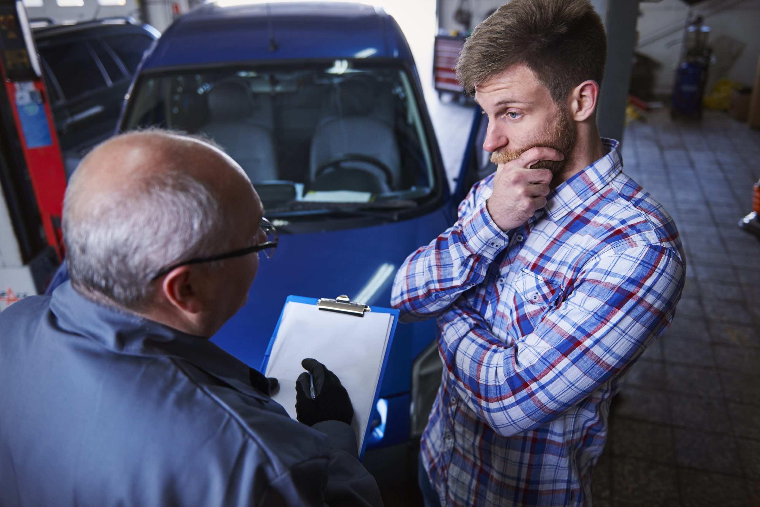 Mechanic taking notes on a clipboard while helping a customer check for a car recall.