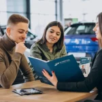 a couple looking over loan terms with an auto financing agent to get pre-approved for a car loan before purchasing a vehicle.