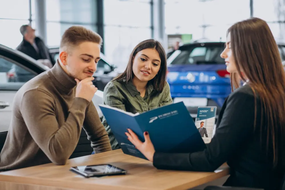a couple looking over loan terms with an auto financing agent to get pre-approved for a car loan before purchasing a vehicle.