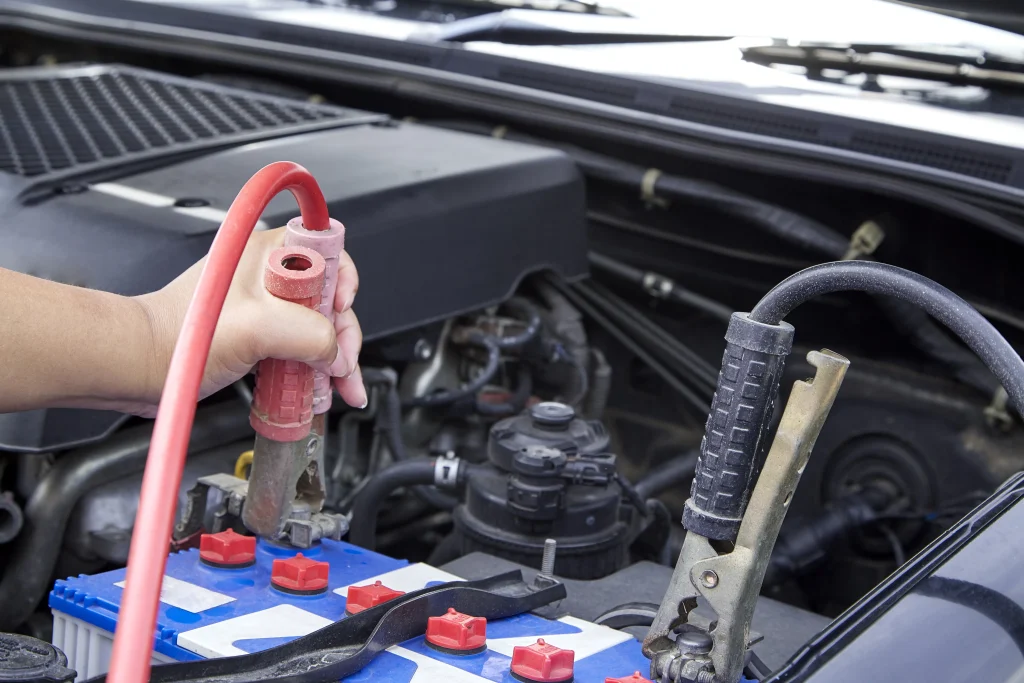 Connecting red and black jumper cables to a car battery for a jump start.