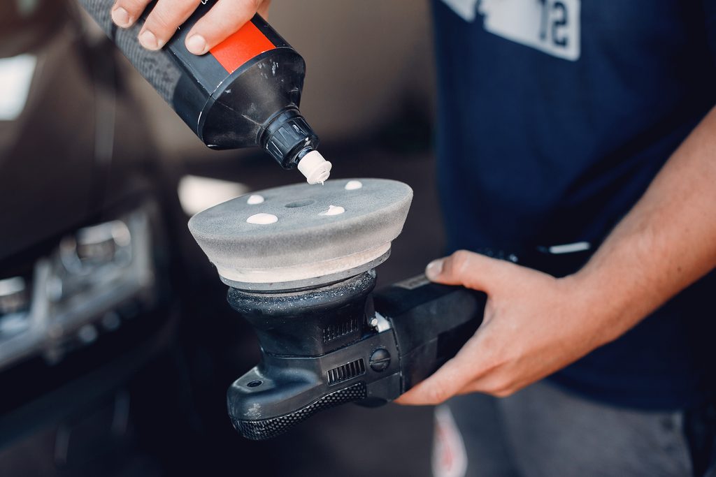 Detailer applying dots of car polishing compound onto a foam pad on a dual-action polisher.