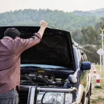 Driver inspecting an open hood to learn how to jump start a car battery after a breakdown.