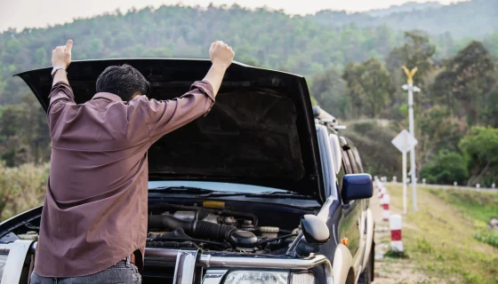 Driver inspecting an open hood to learn how to jump start a car battery after a breakdown.