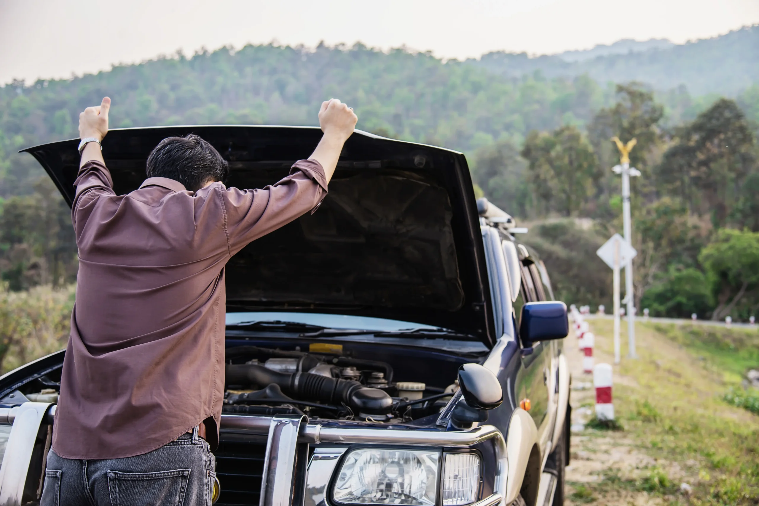 Driver inspecting an open hood to learn how to jump start a car battery after a breakdown.