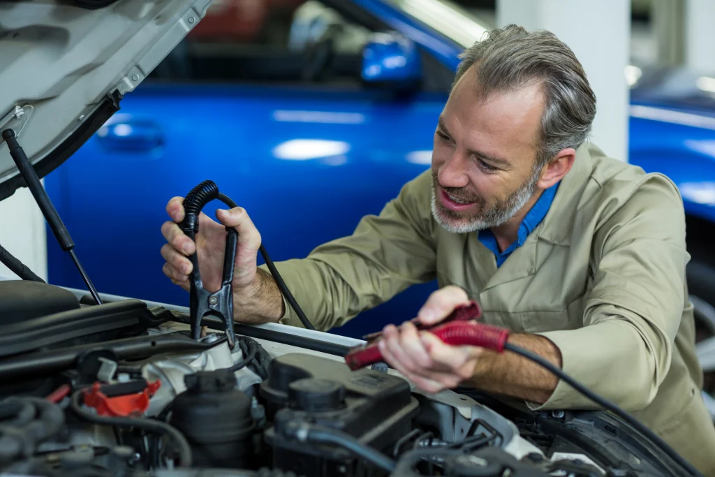 Mechanic attaching red clamp and grounding black lead to jump start a car battery.