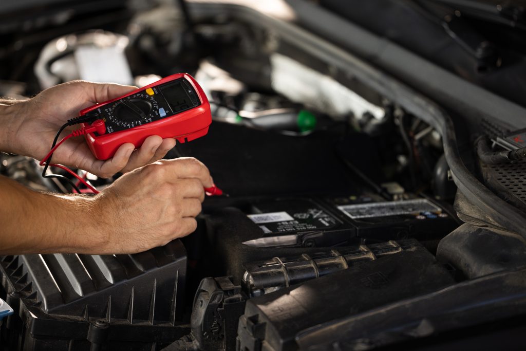 Close-up of hands placing red and black multimeter probes on car battery terminals to test voltage.