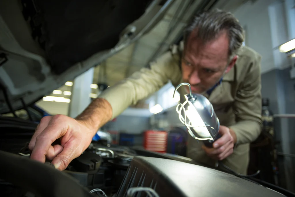Mechanic inspecting car engine parts with a work light before attempting to jump start a car battery.