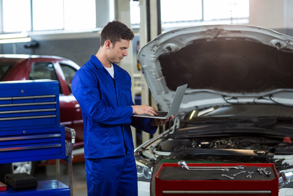 Service technician checking chassis code database on a laptop at an authorized distributor center to check for a car recall.