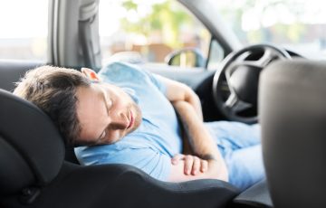 A man sleeping peacefully on a reclined front seat, showing how to sleep comfortably in a car during a long road trip or rest stop.