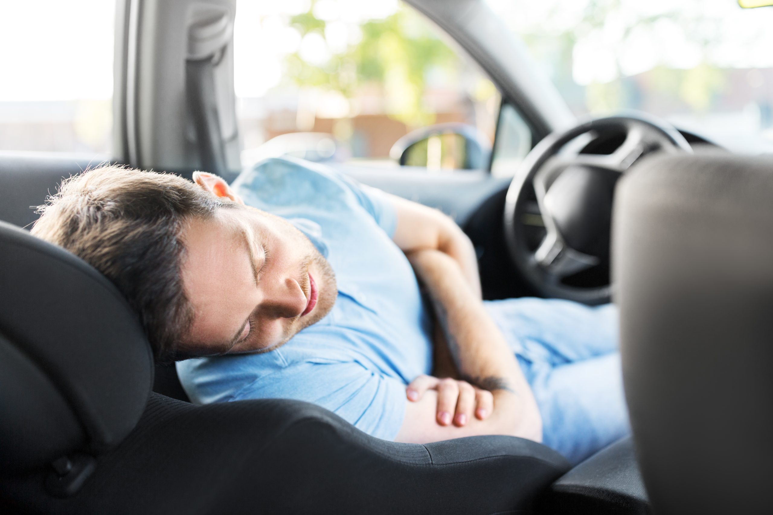 A man sleeping peacefully on a reclined front seat, showing how to sleep comfortably in a car during a long road trip or rest stop.