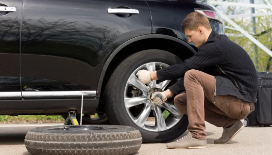 A driver learning how to change a car tire with a lug wrench and scissor jack.