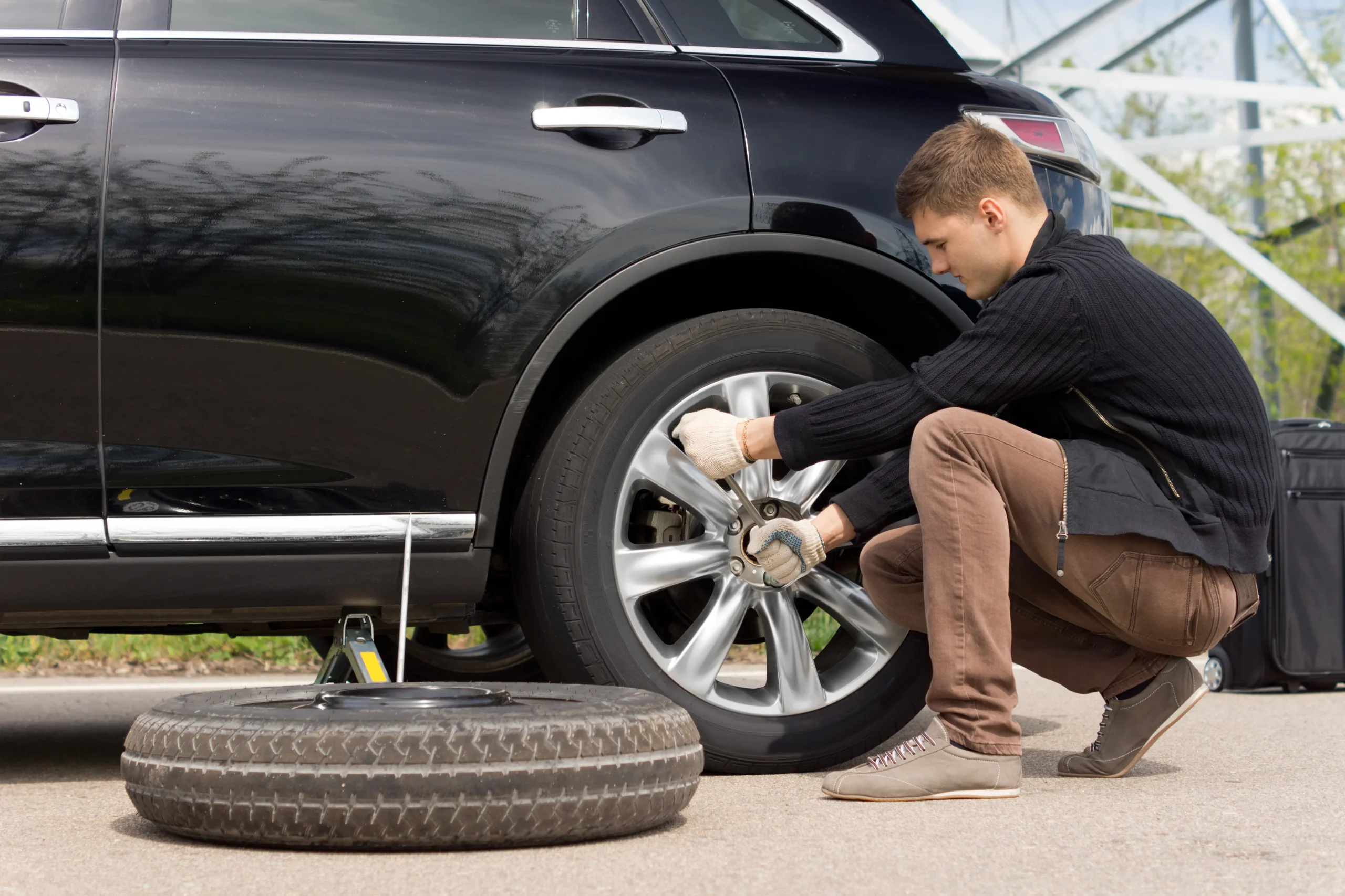 A driver learning how to change a car tire with a lug wrench and scissor jack.